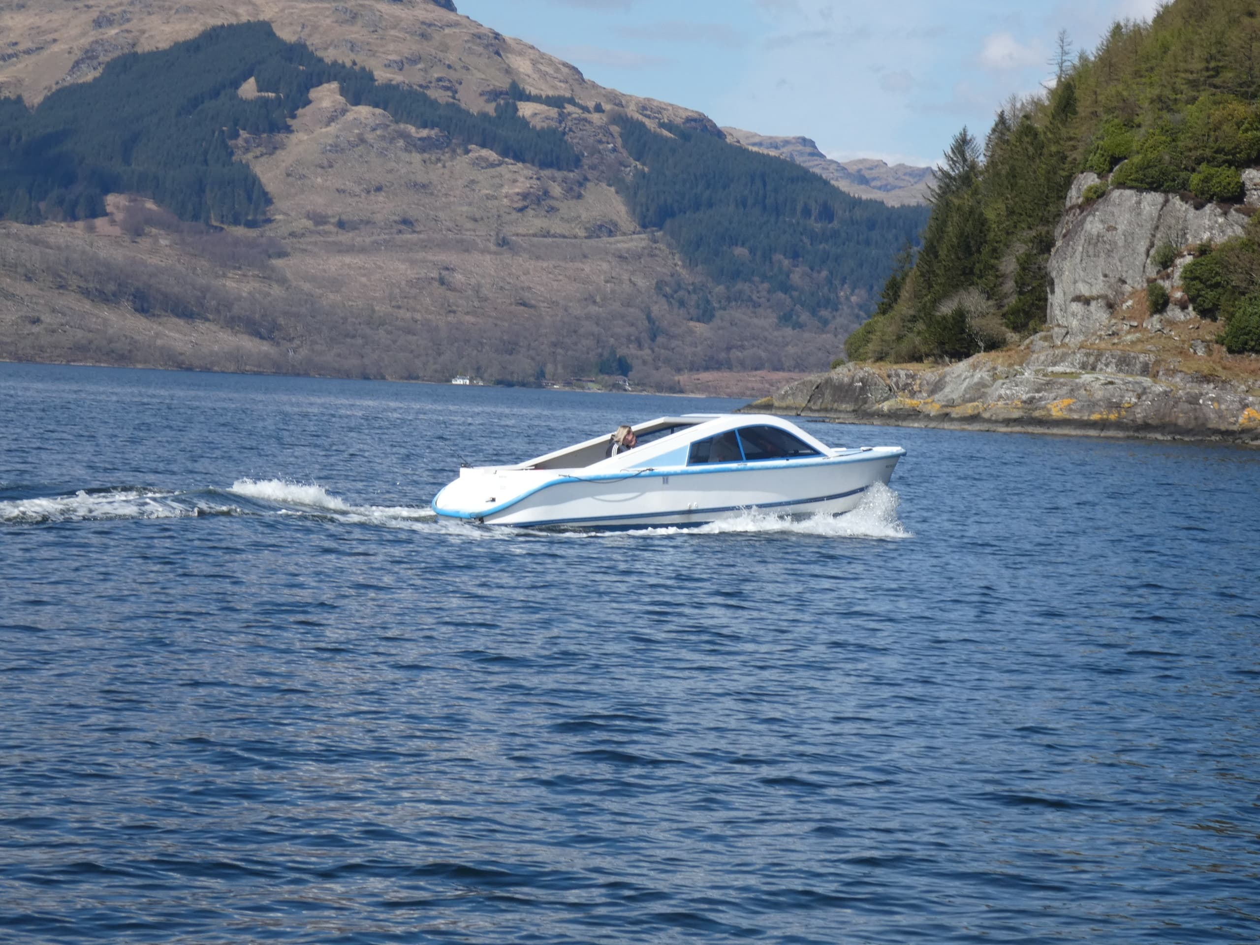 Speedboat cruising on Loch Goil with mountain shoreline