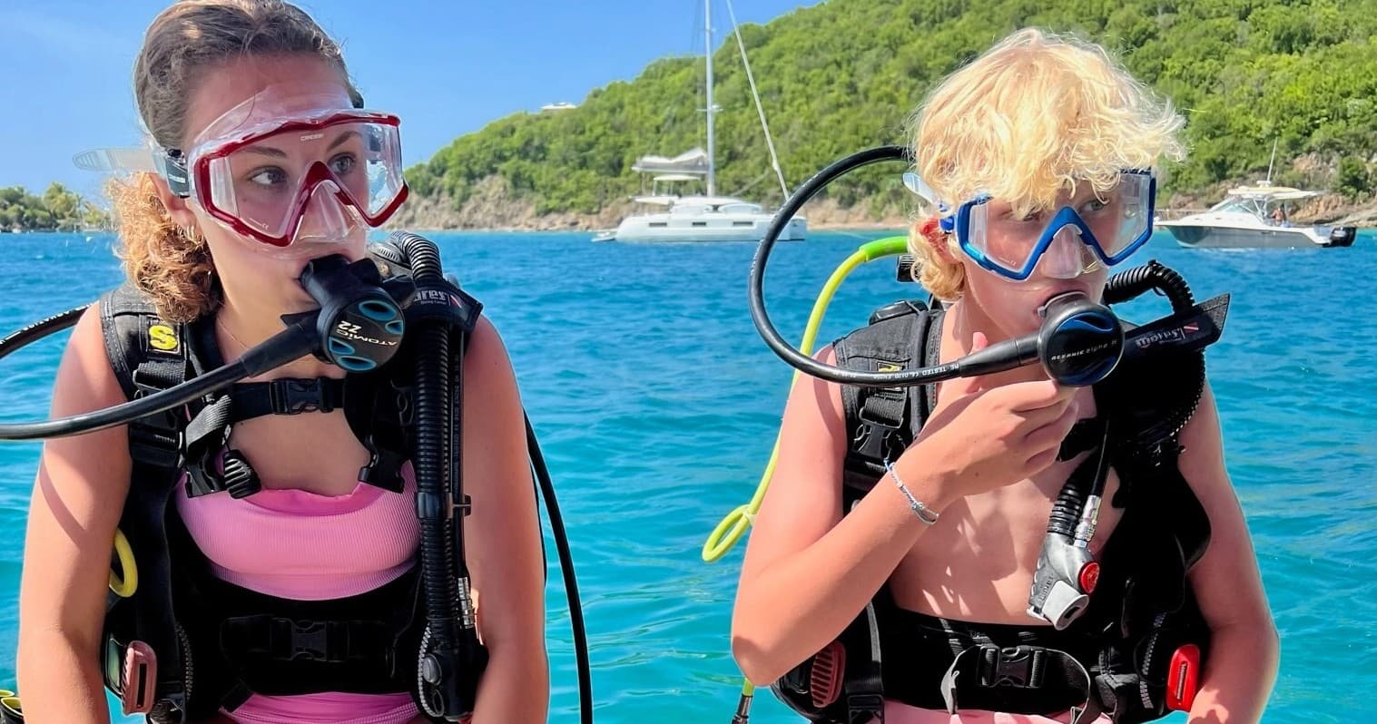 Two snorkelers preparing scuba gear on boat near tropical shore