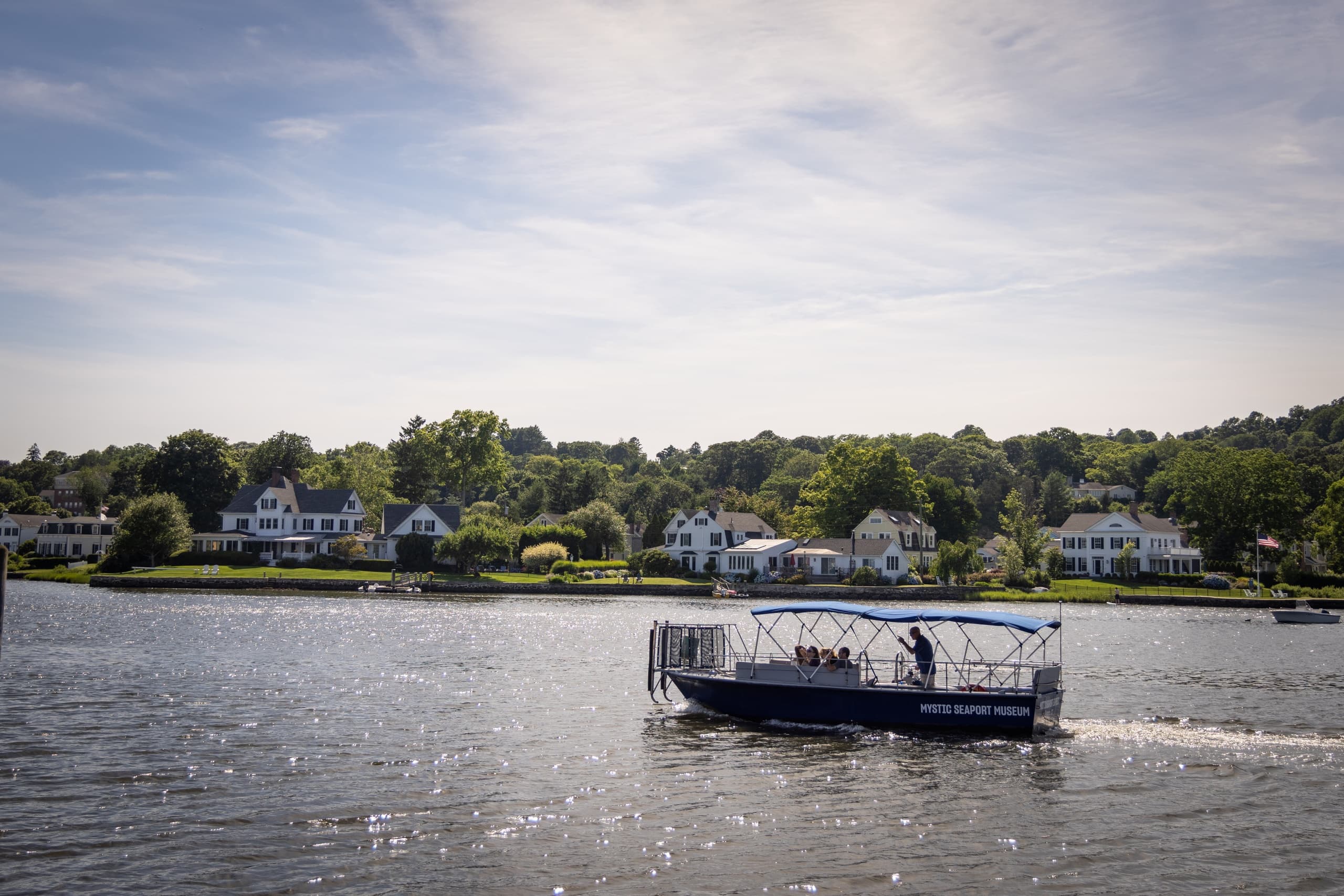 Open passenger ferry cruising across calm river with shoreline homes