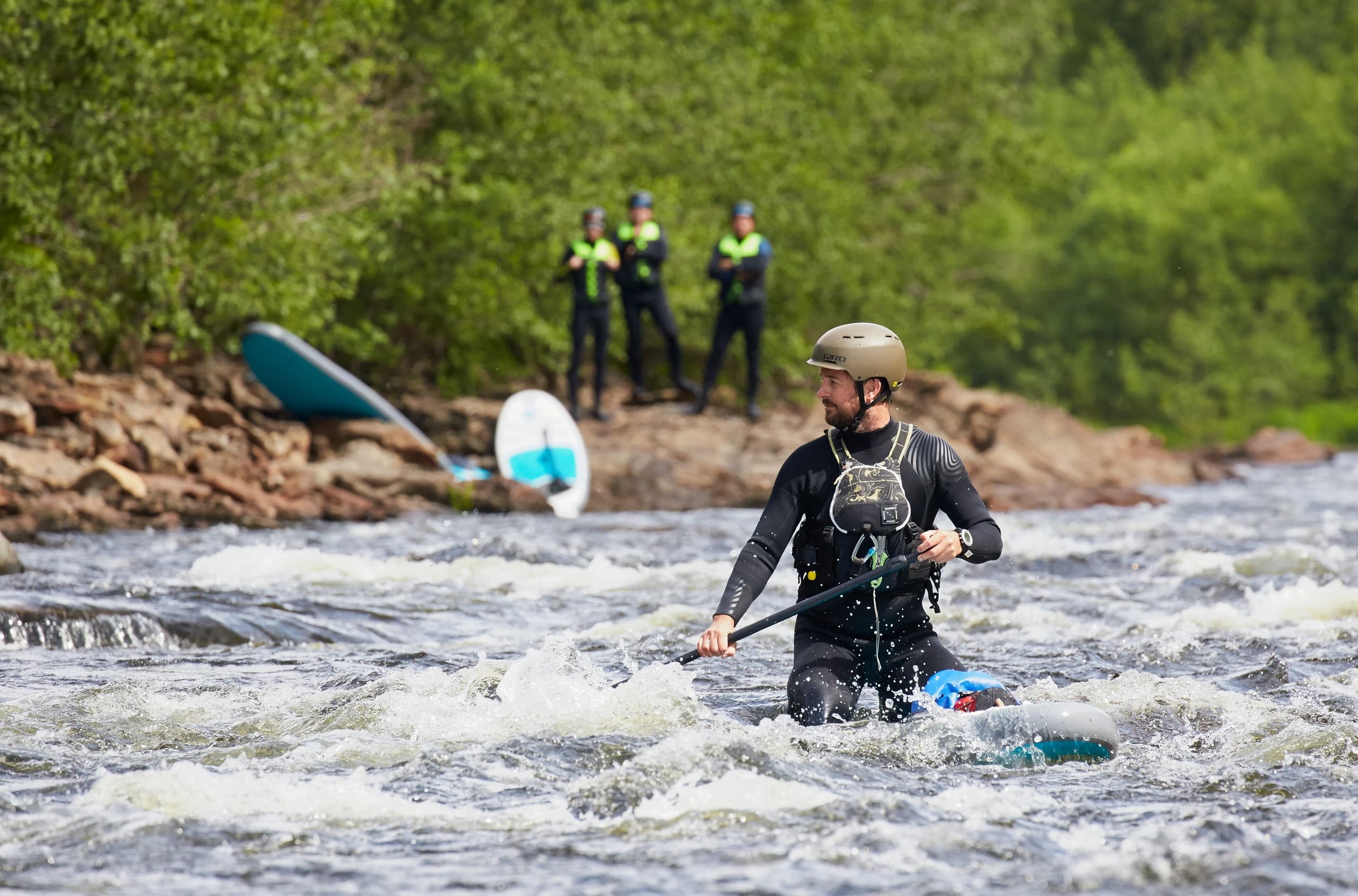 Guide wading with paddle through choppy whitewater near rocky shore