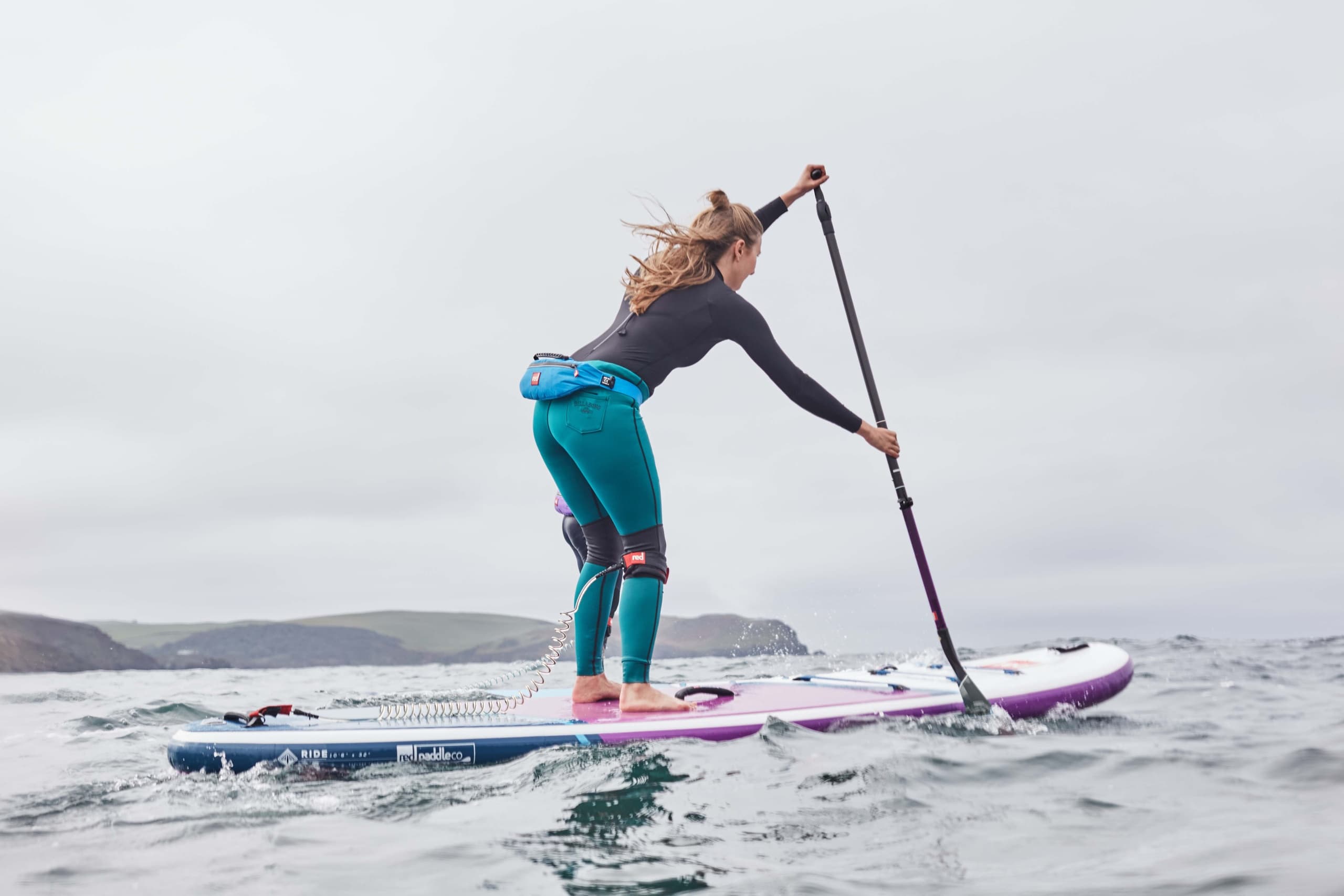 Woman stand-up paddleboarding on open sea near cliffs