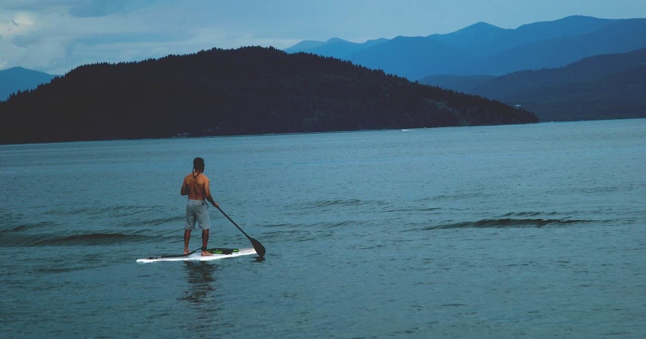 Stand-up paddleboarding on calm mountain lake at dusk