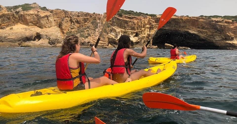 Kayakers paddling yellow tandem kayak along coastal cliffs