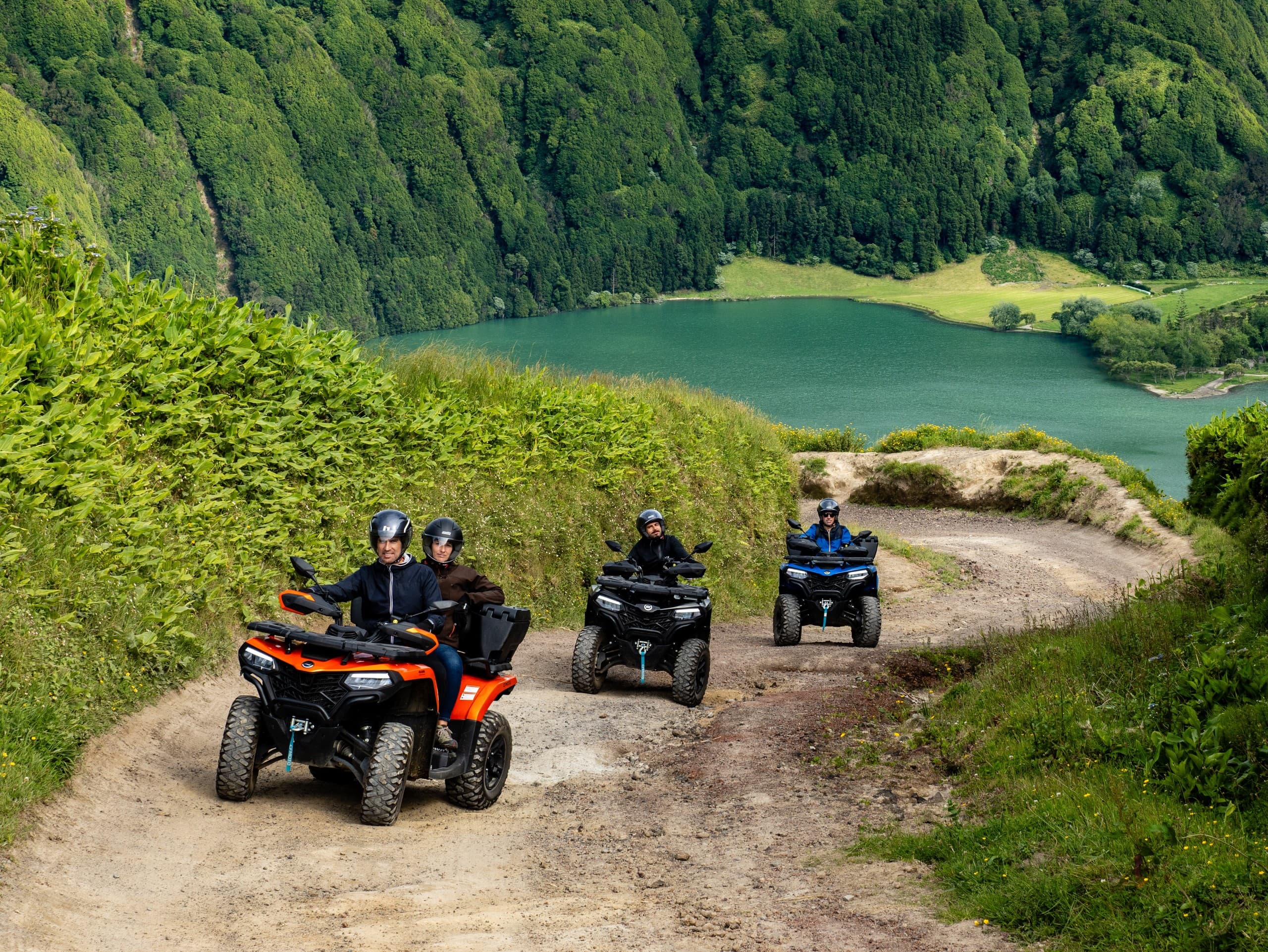Three off-road buggies driving mountain trail above lake