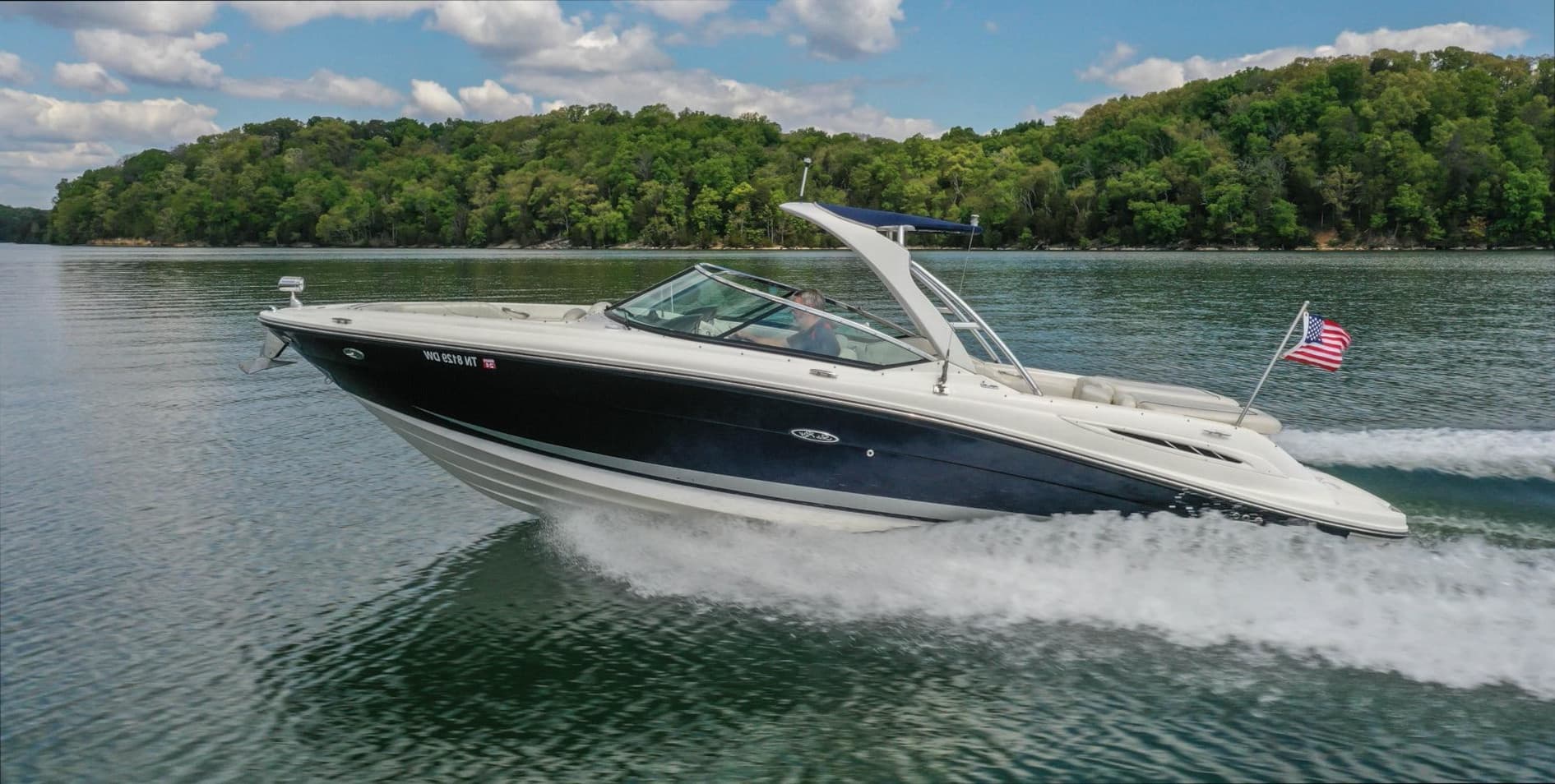 Speedboat powering across lake with shoreline and trees