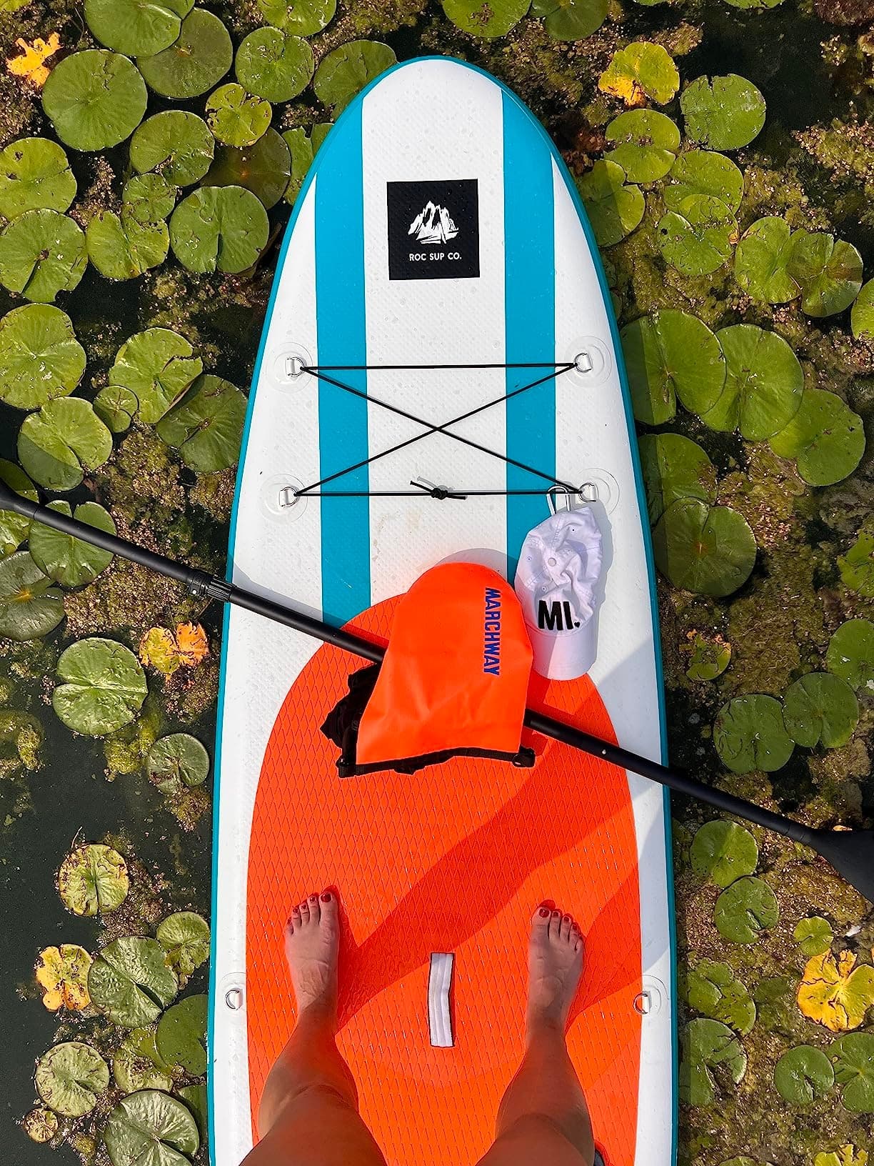 Stand-up paddleboard over lily pads, feet on deck, calm water