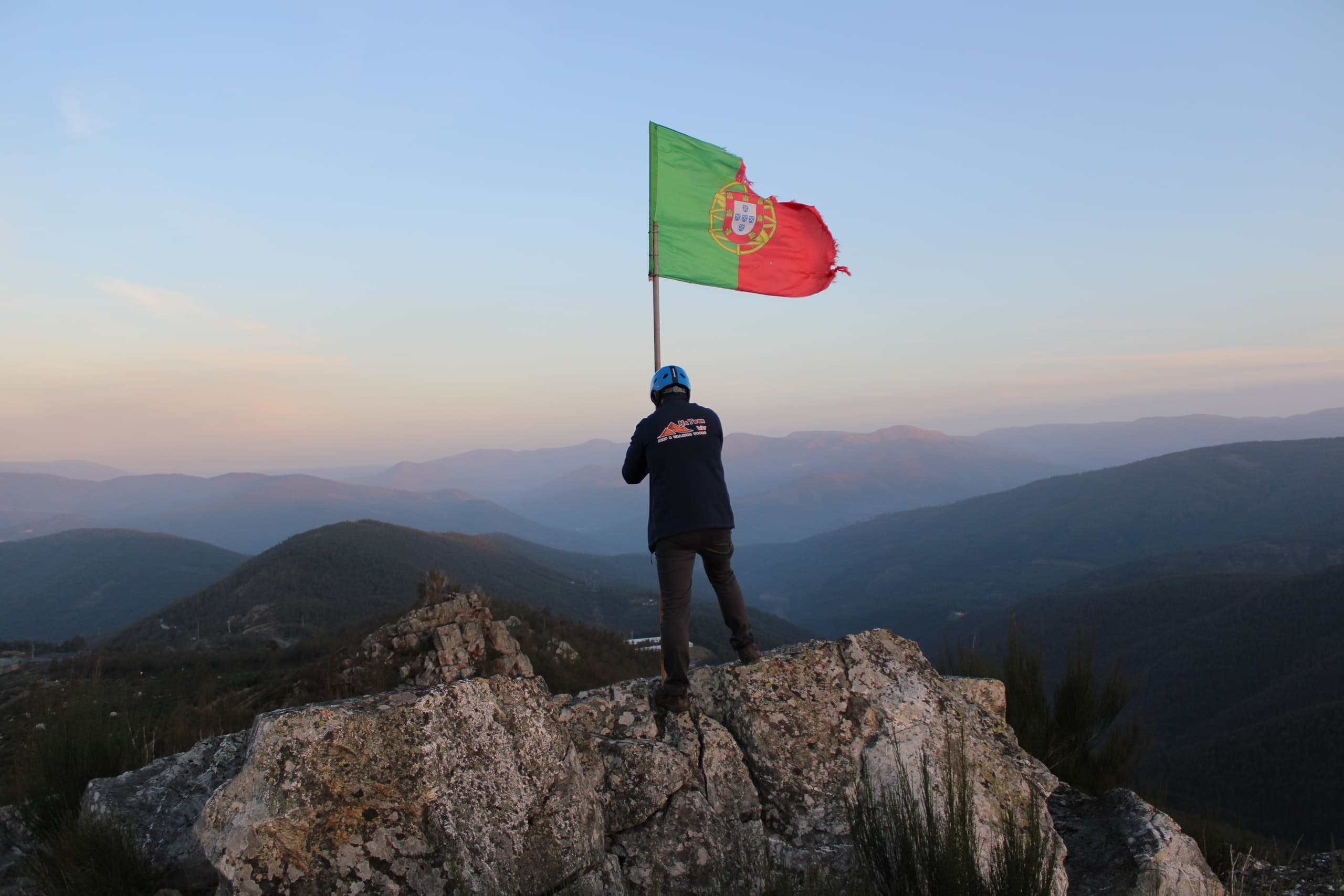 Hiker waving Portuguese flag on mountain summit at sunset