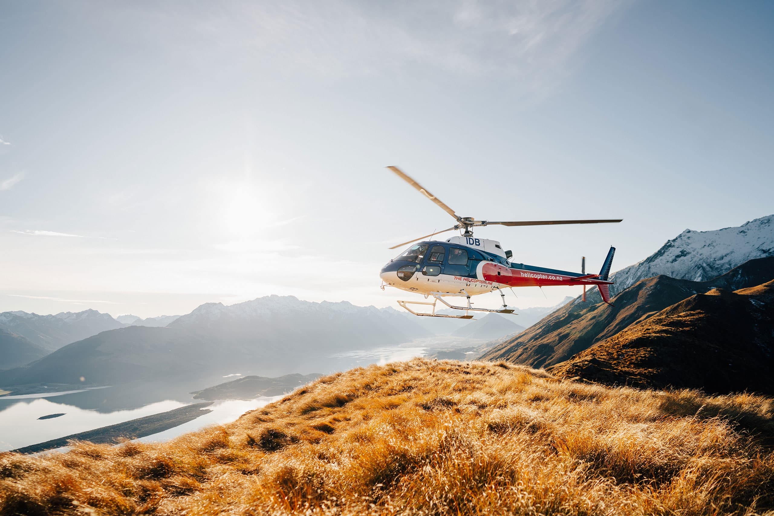 Helicopter flying over alpine ridgeline and golden tussock at sunrise