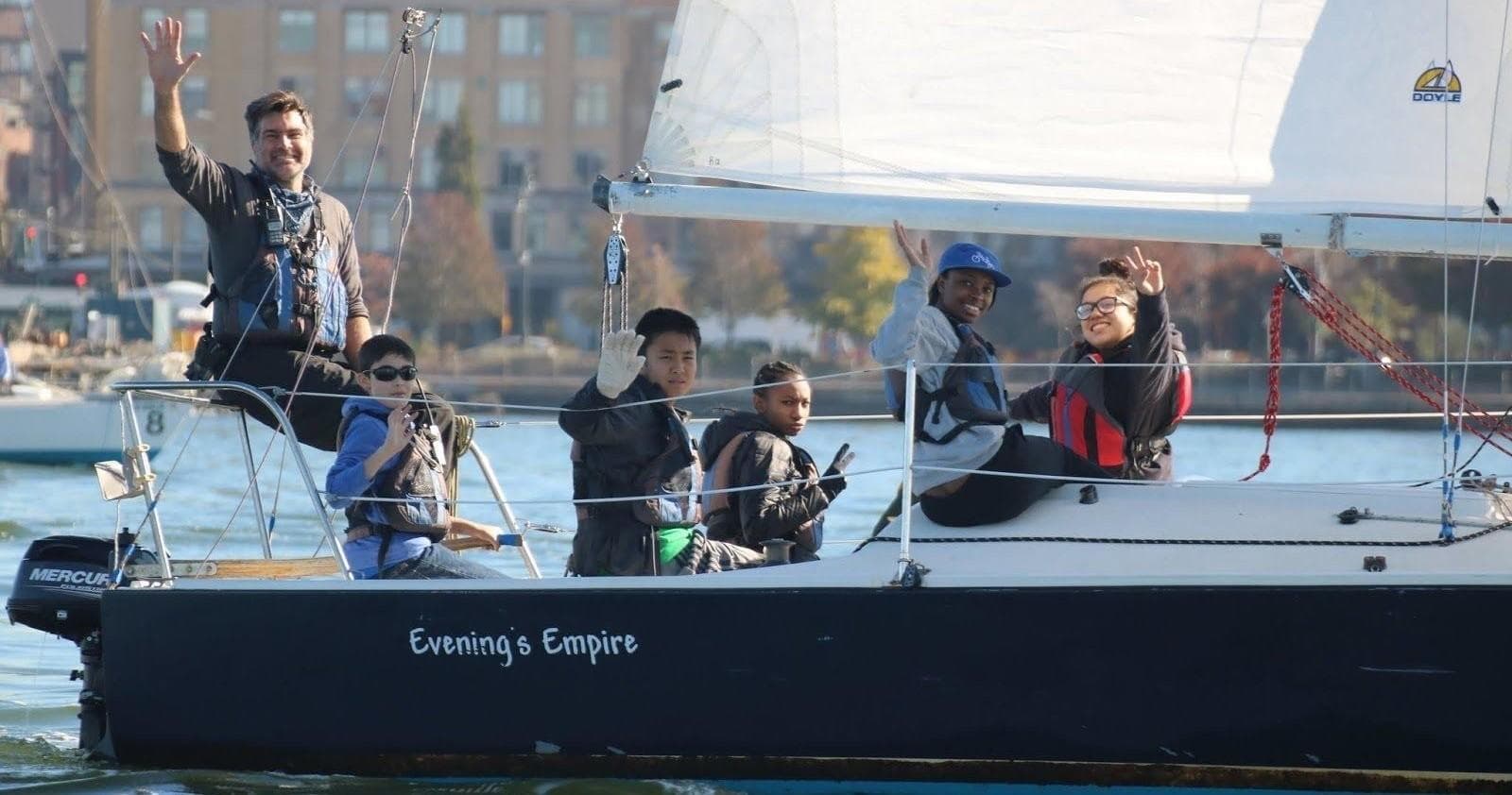 Family and kids waving aboard cruising sailboat on the river