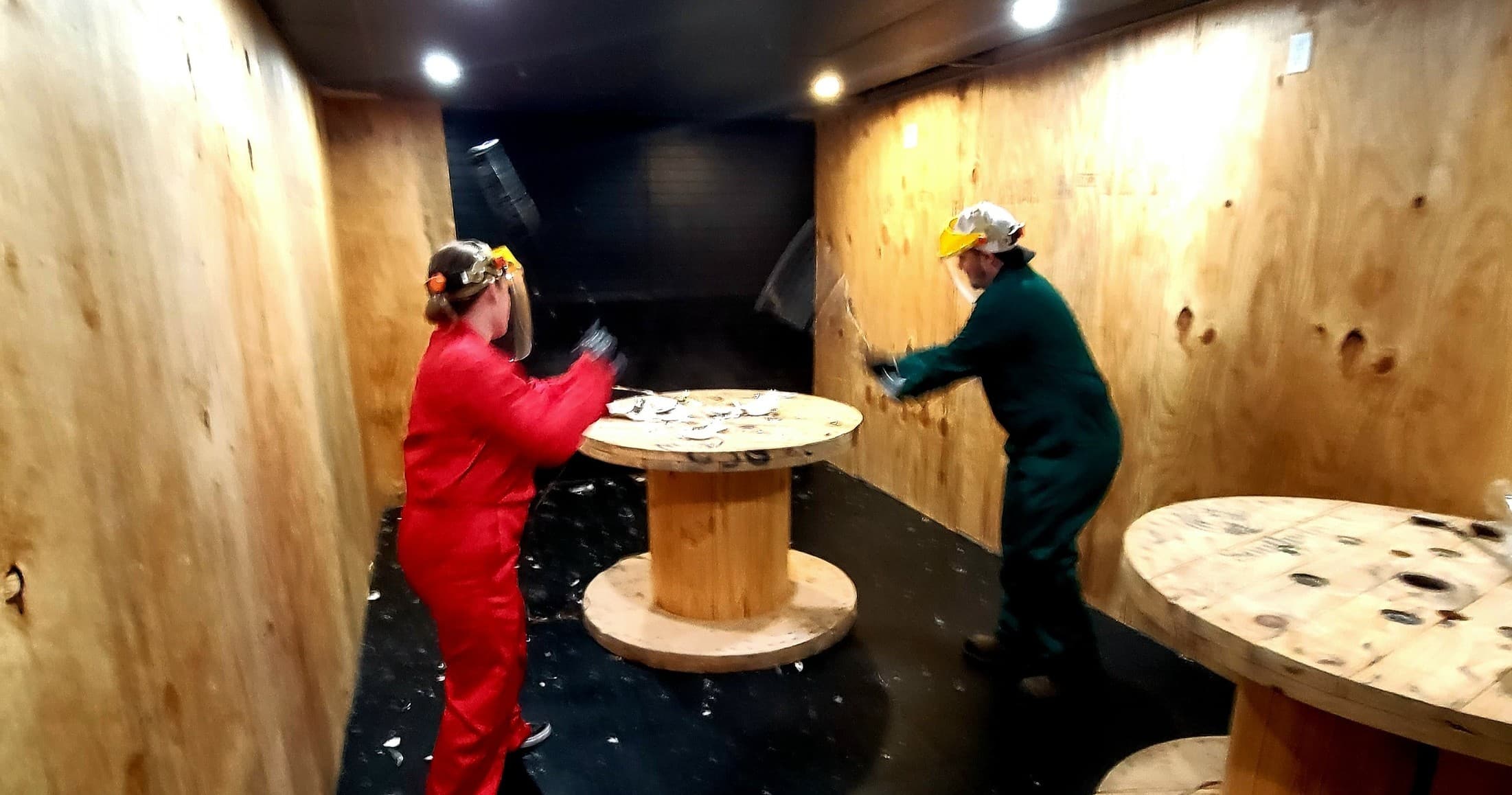 Participants smashing objects in indoor rage room with wooden walls