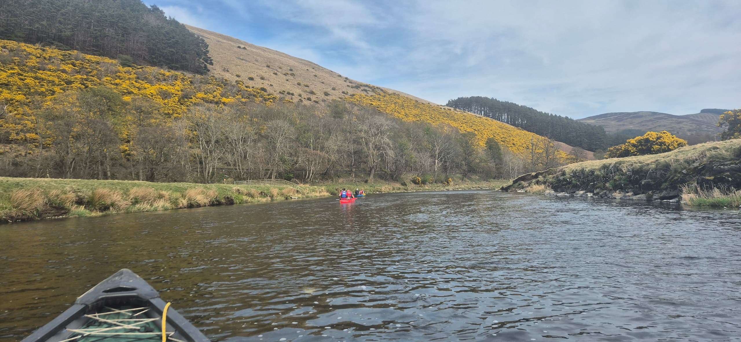Paddler's view from a canoe down a wide river through hills