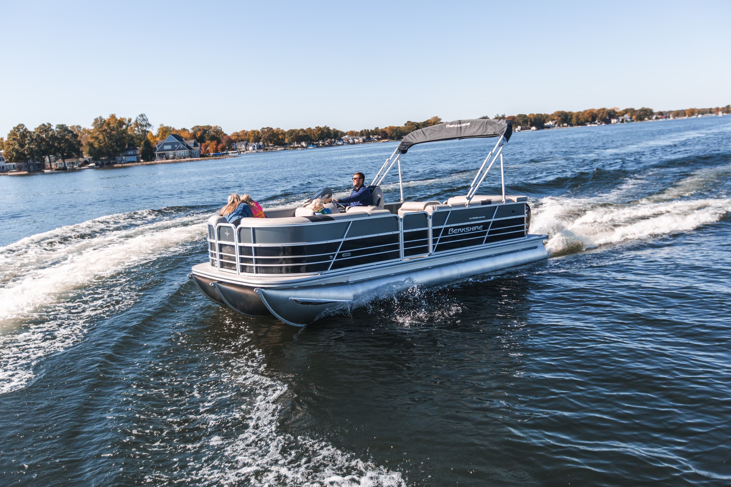 Pontoon boat cruising on lake with shoreline homes and wake