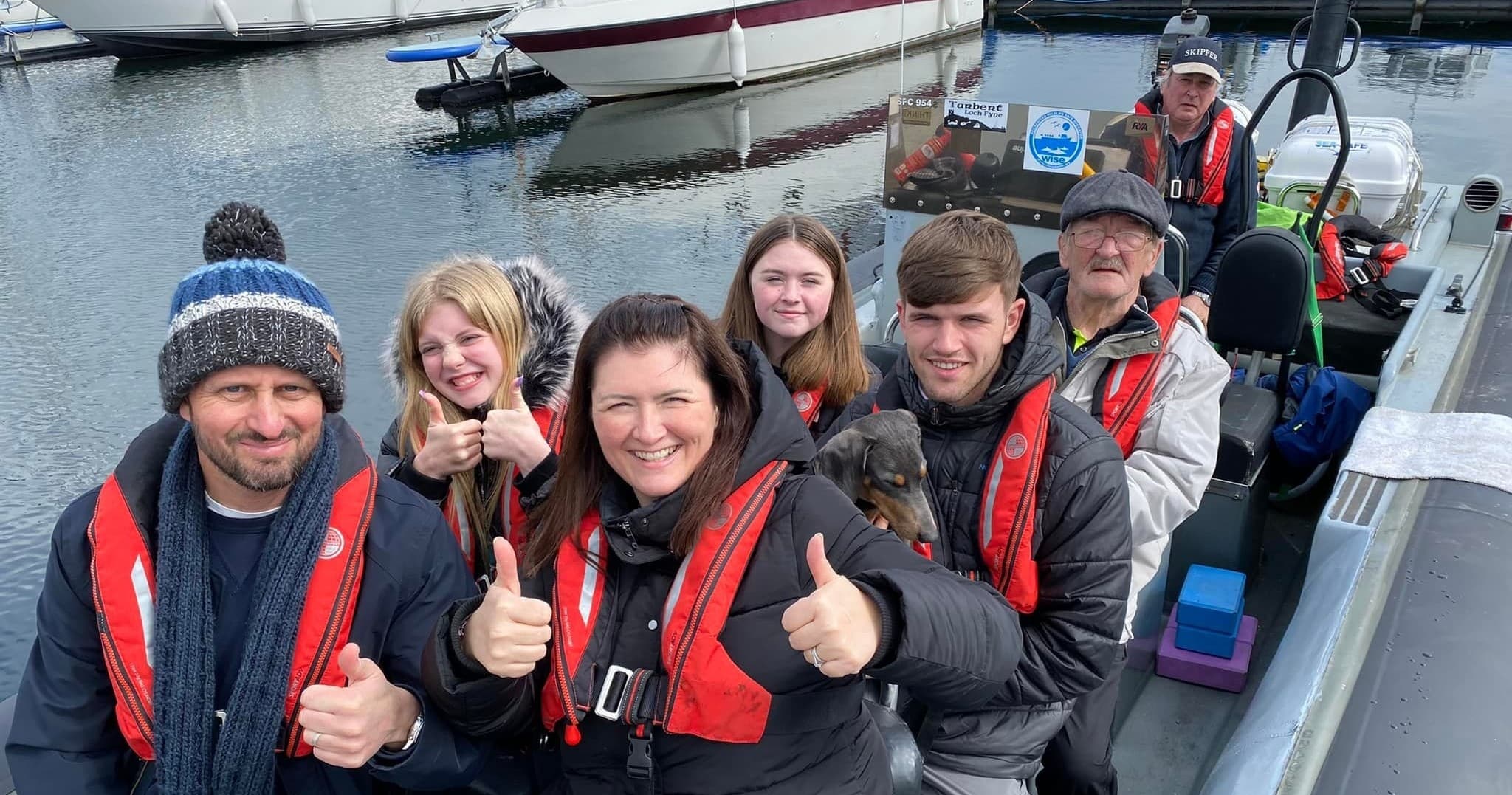 Happy tour group aboard RIB boat wearing lifejackets at harbor