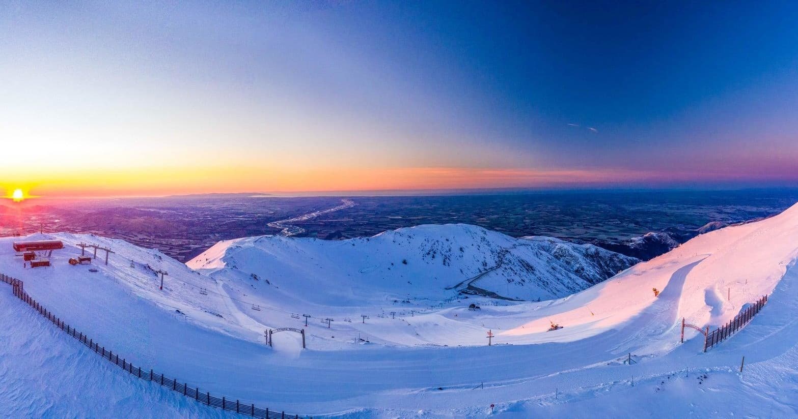 Sunrise over snow-covered ski slopes and chairlifts, alpine vista