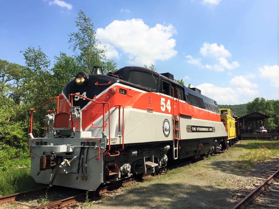 Red heritage locomotive cruising past green fields under blue sky
