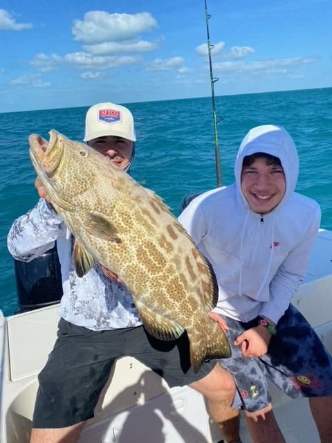 Young anglers holding giant grouper on blue ocean nearshore charter