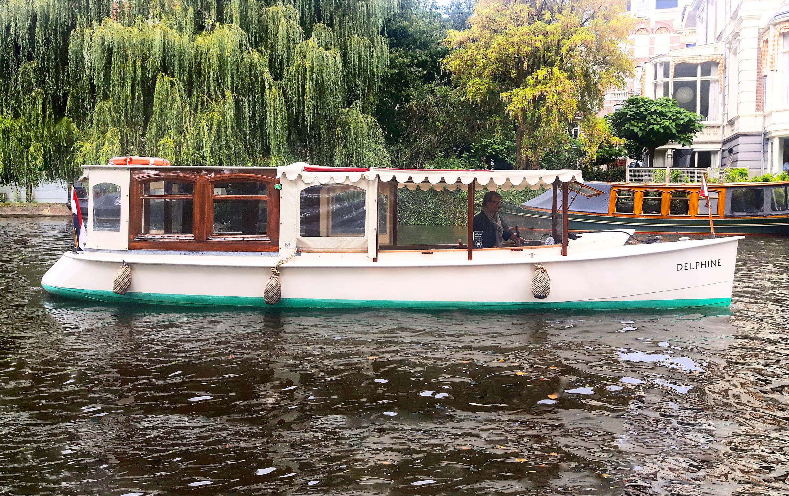 Sightseeing boat cruising a leafy Amsterdam canal tour scene