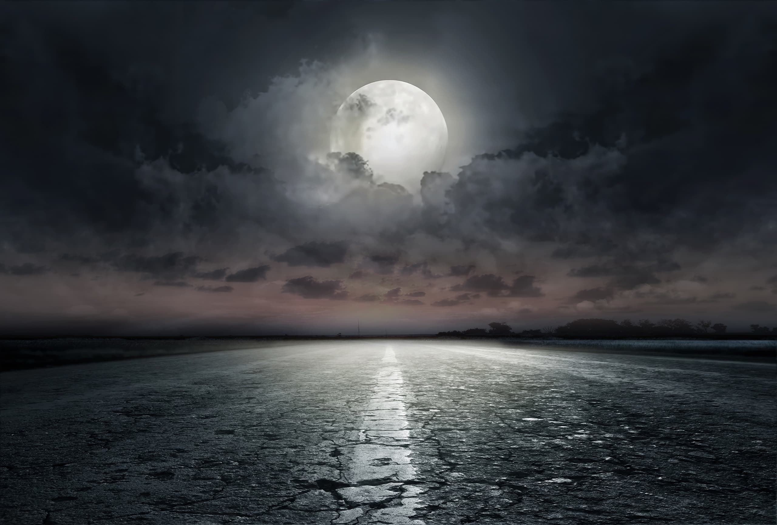 Moonlit open road stretching to horizon under cloudy sky