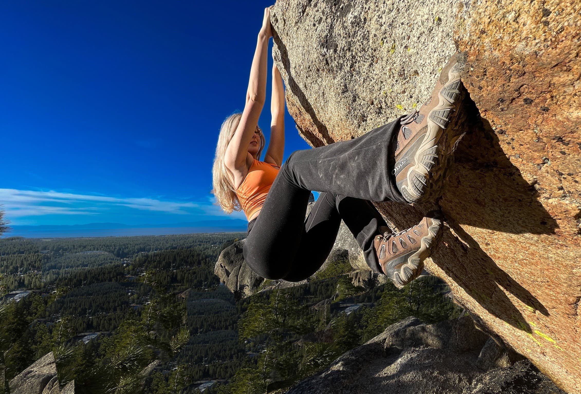 Climber bouldering overhang above forested Sierra Nevada vista