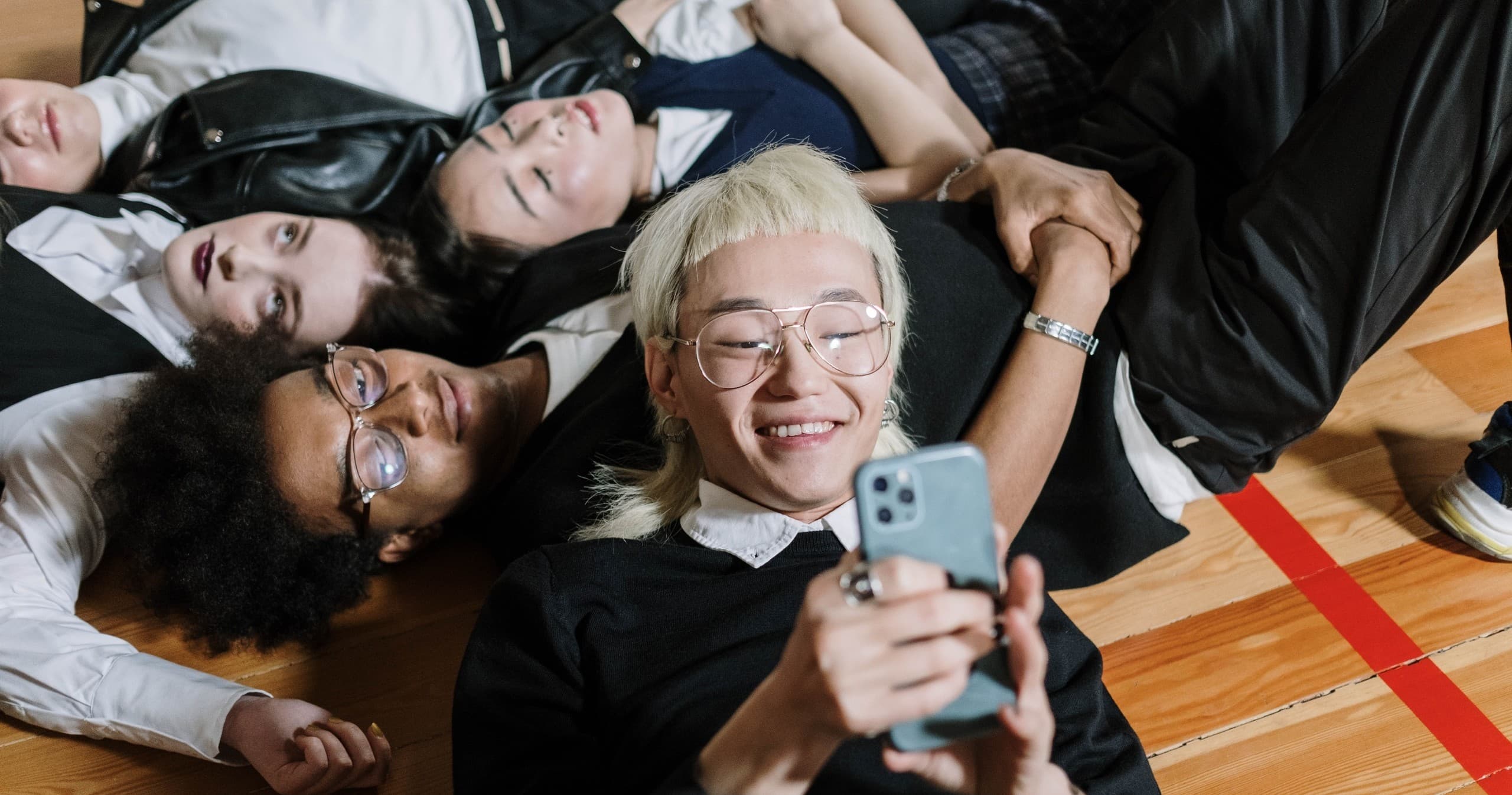 Group of friends lying on gym floor taking playful group selfie