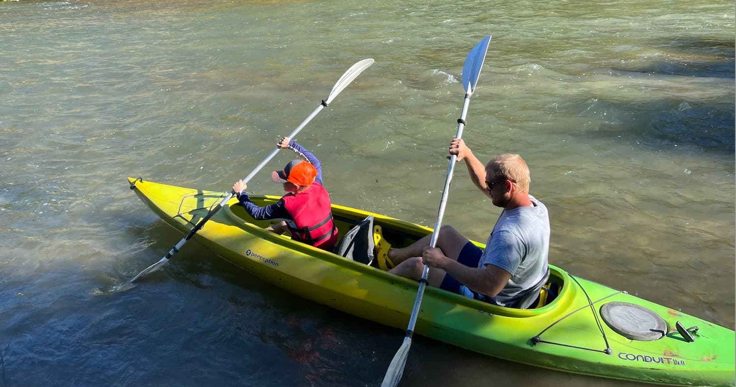 Tandem kayakers paddling on a calm river near shore