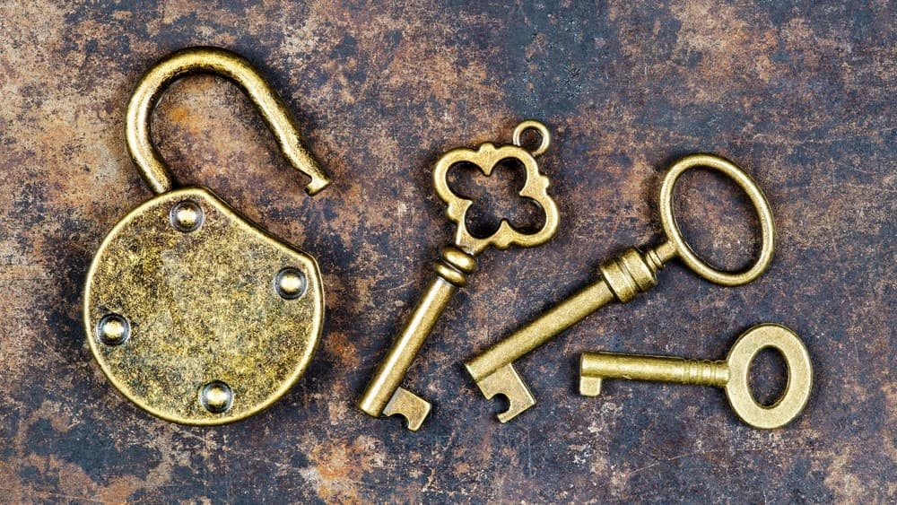 Antique brass keys and open padlock laid on a rustic metal surface