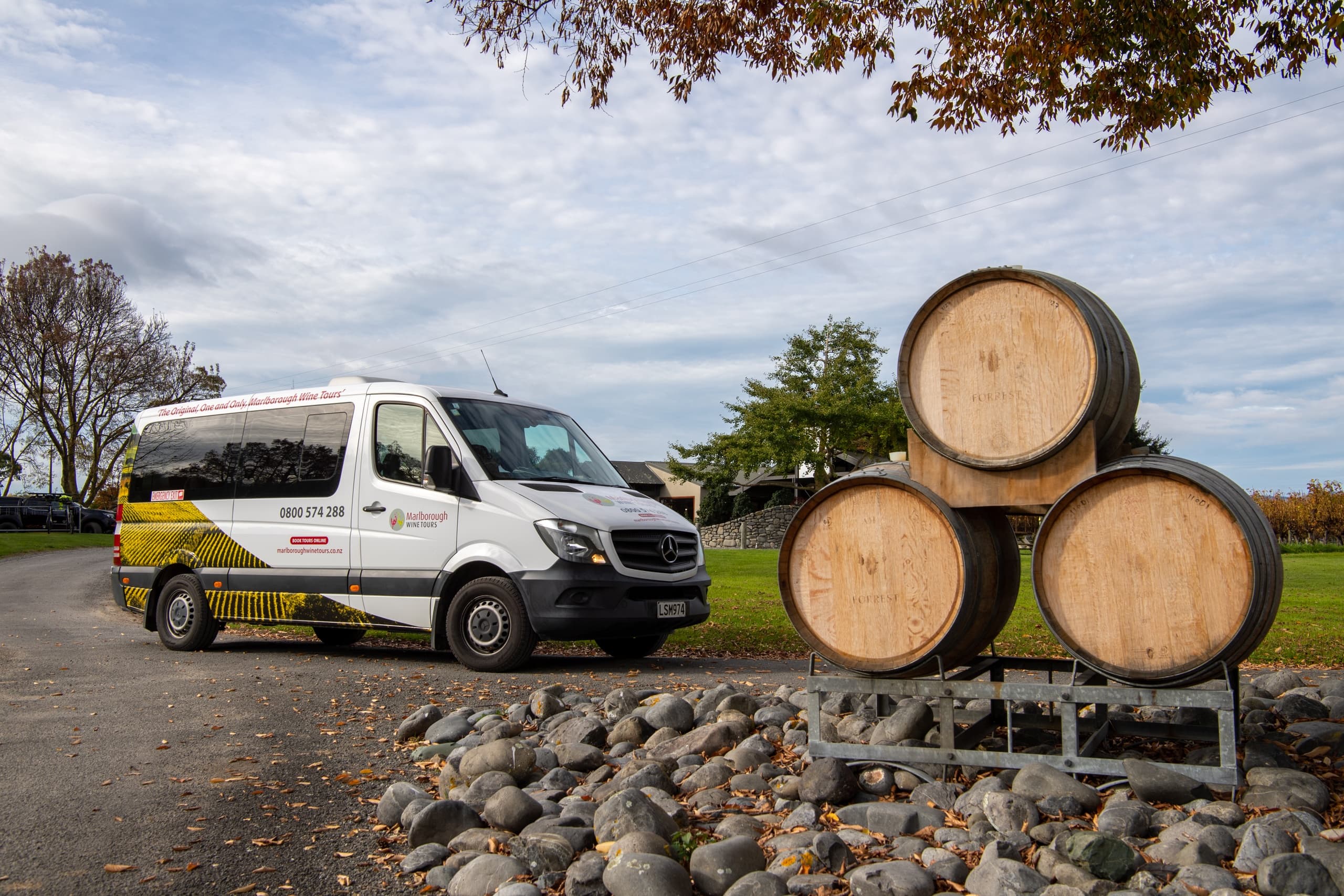 Stacked wine barrels beside vineyard with shuttle van outdoors