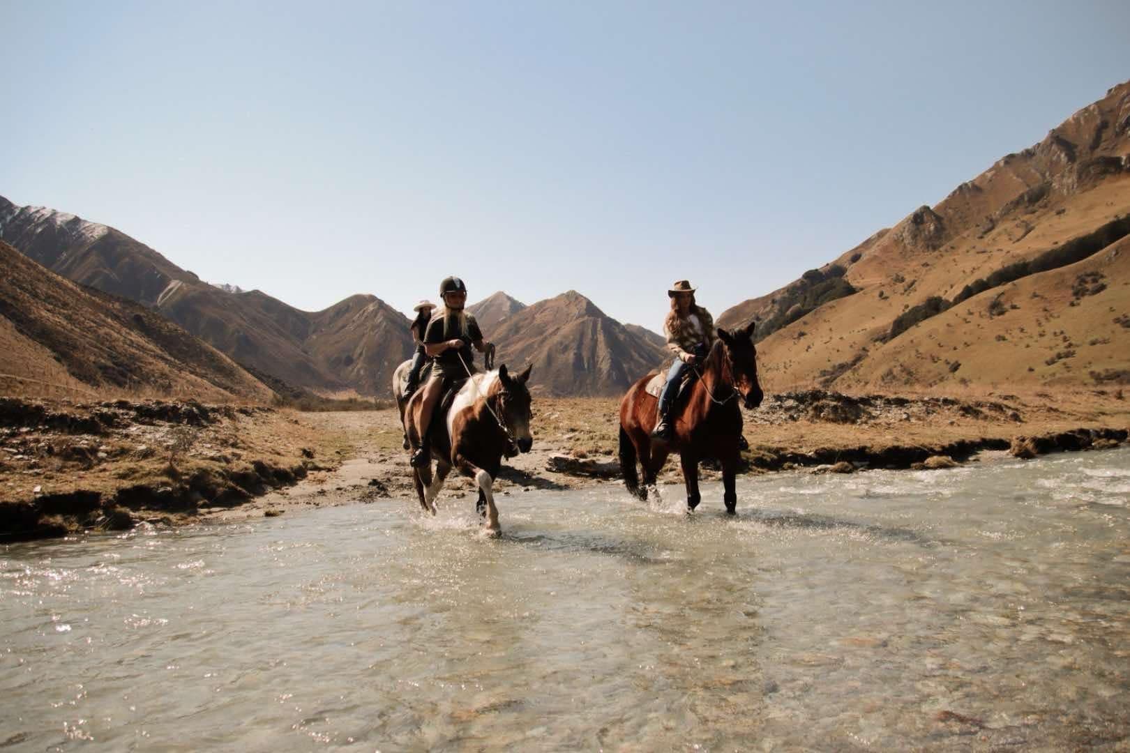 Two horseback riders splashing through shallow alpine stream