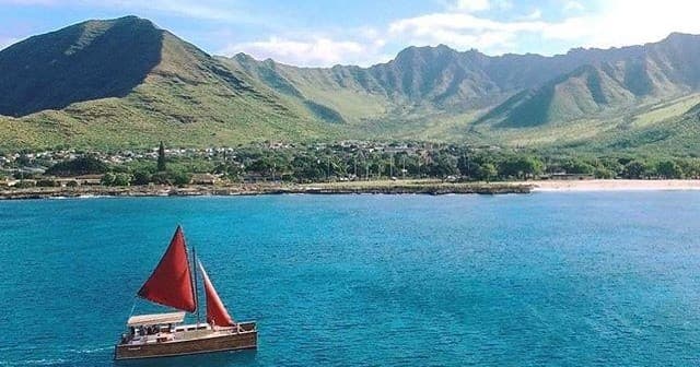 Traditional sailboat with red sail near green shoreline