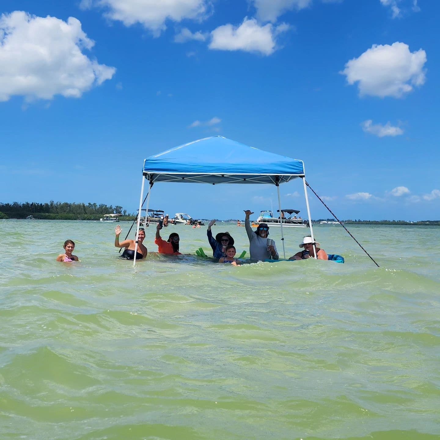 Group relaxing under canopy in shallow emerald coastal waters