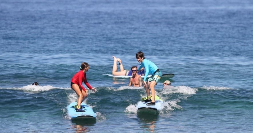 Students practicing standing on surfboards in calm ocean surf