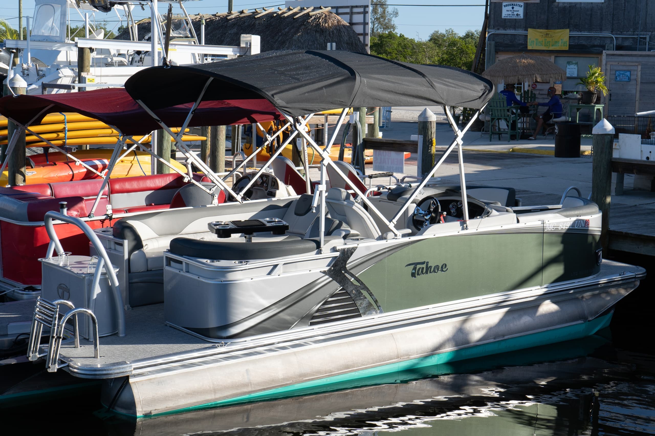 Green pontoon boat tied at busy marina dock with canopy