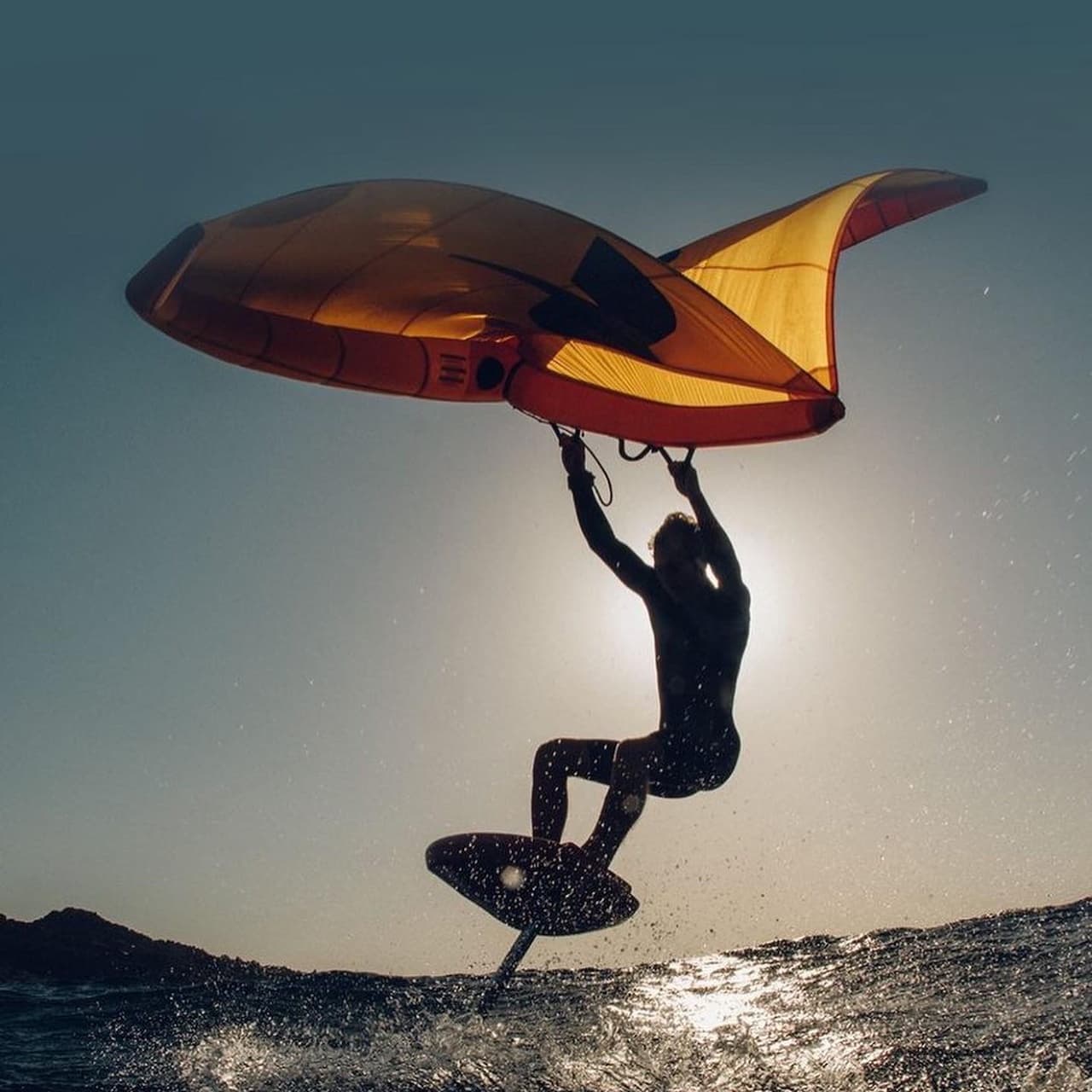 Wingfoil silhouette launching at golden sunset over sea