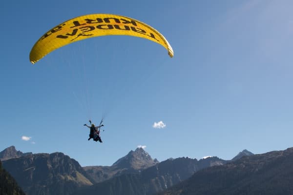 Single paraglider silhouetted over alpine peaks, soaring high