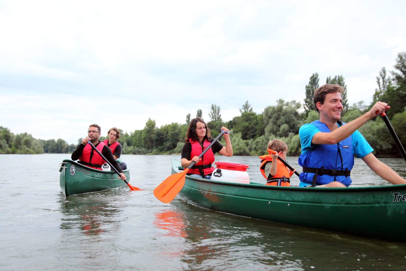 Group canoeing on river with families paddling near shoreline
