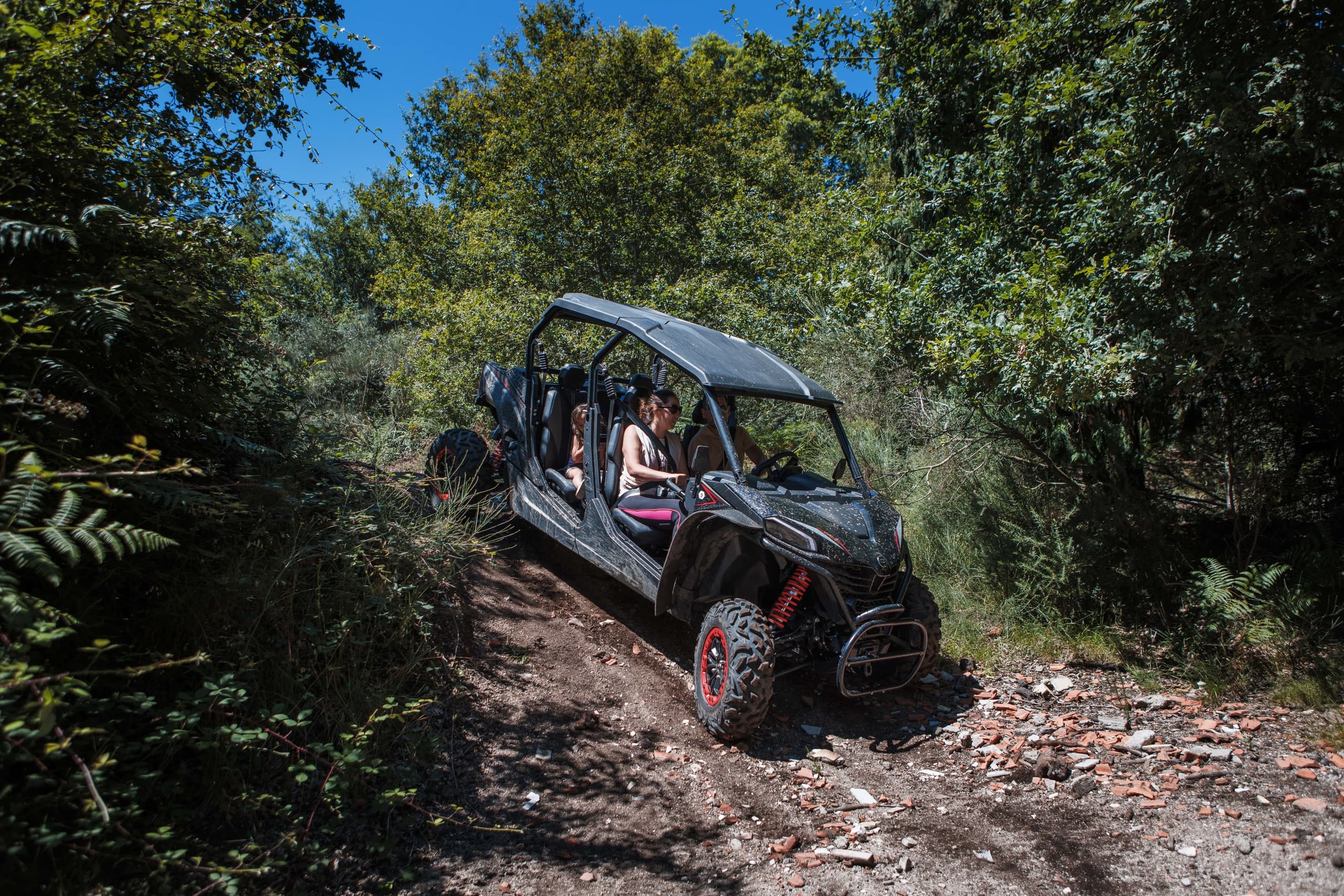 Side-by-side UTV traversing rocky forest trail under trees