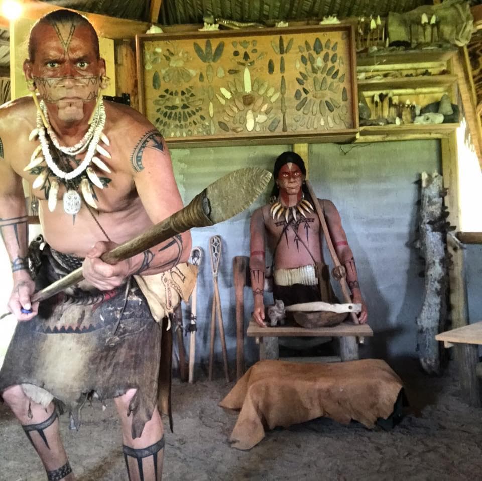 Warrior in traditional attire demonstrating tools inside village hut