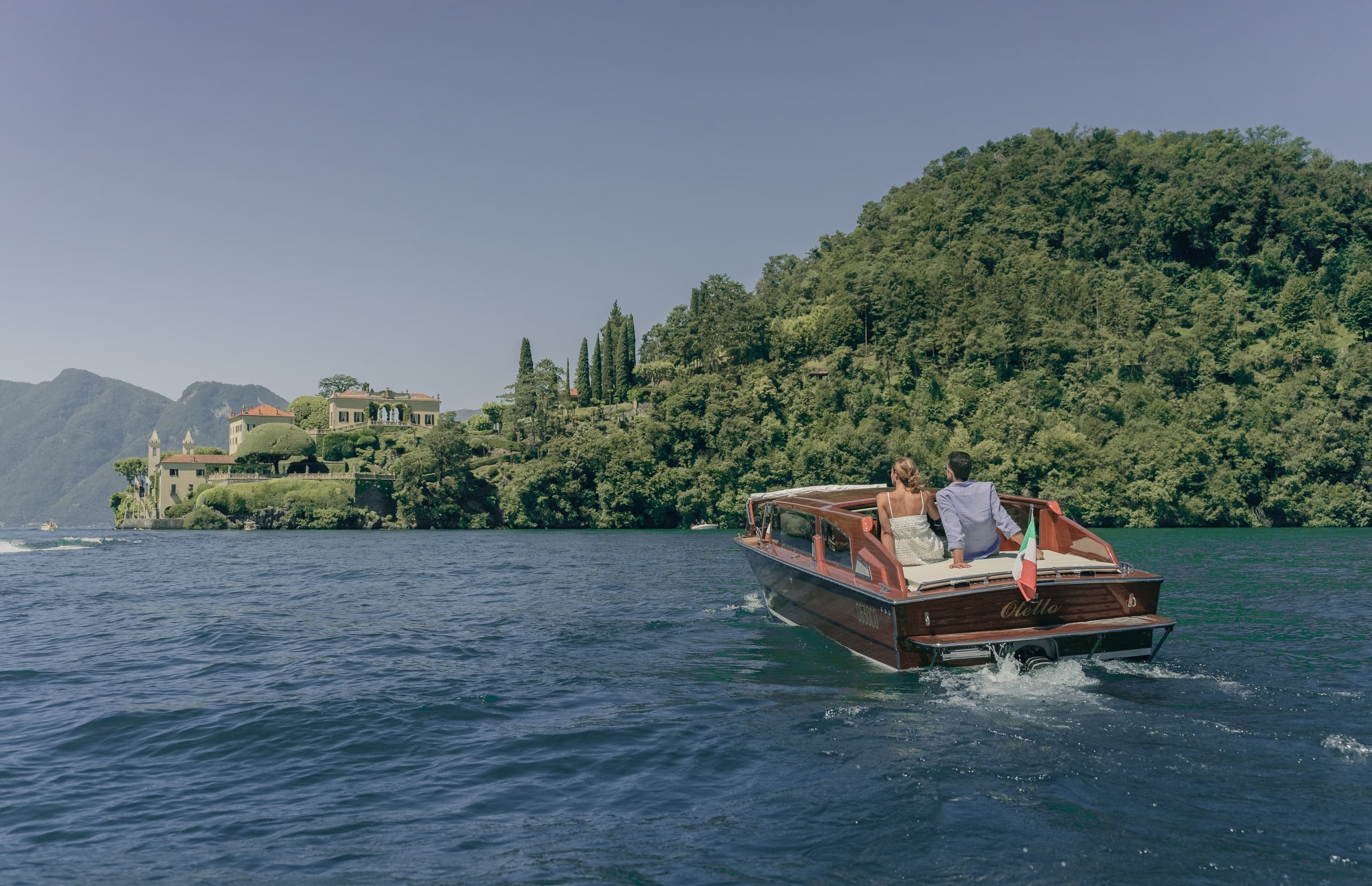 Classic wooden boat cruising Lake Como toward villa shoreline