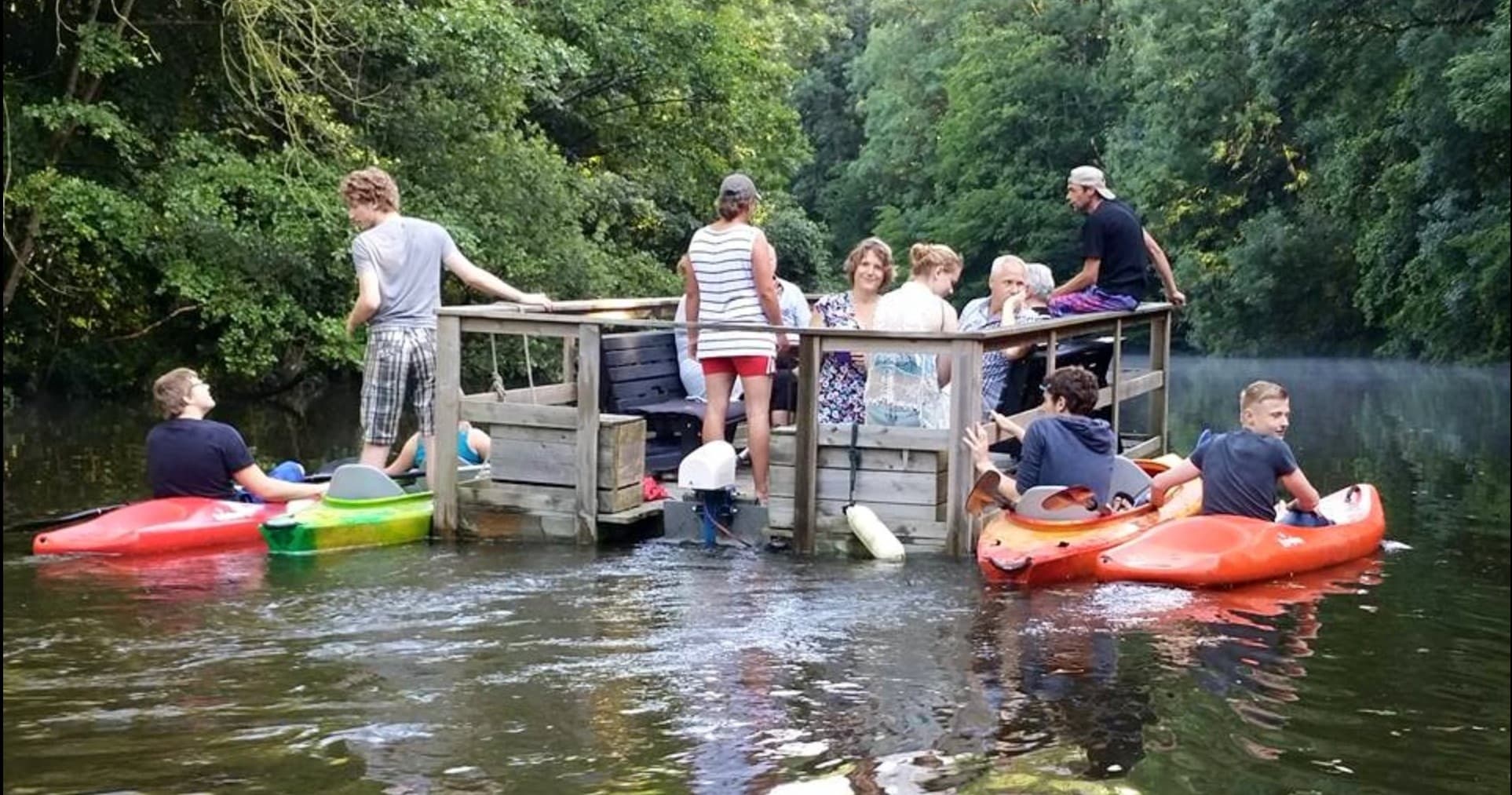 Group launching kayaks from wooden platform on forested river
