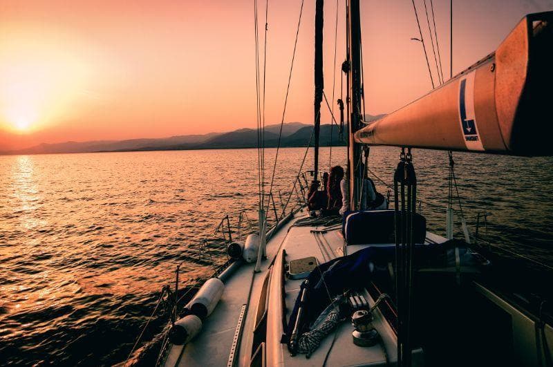 Sailboat cruising at sunset on calm ocean with warm glow