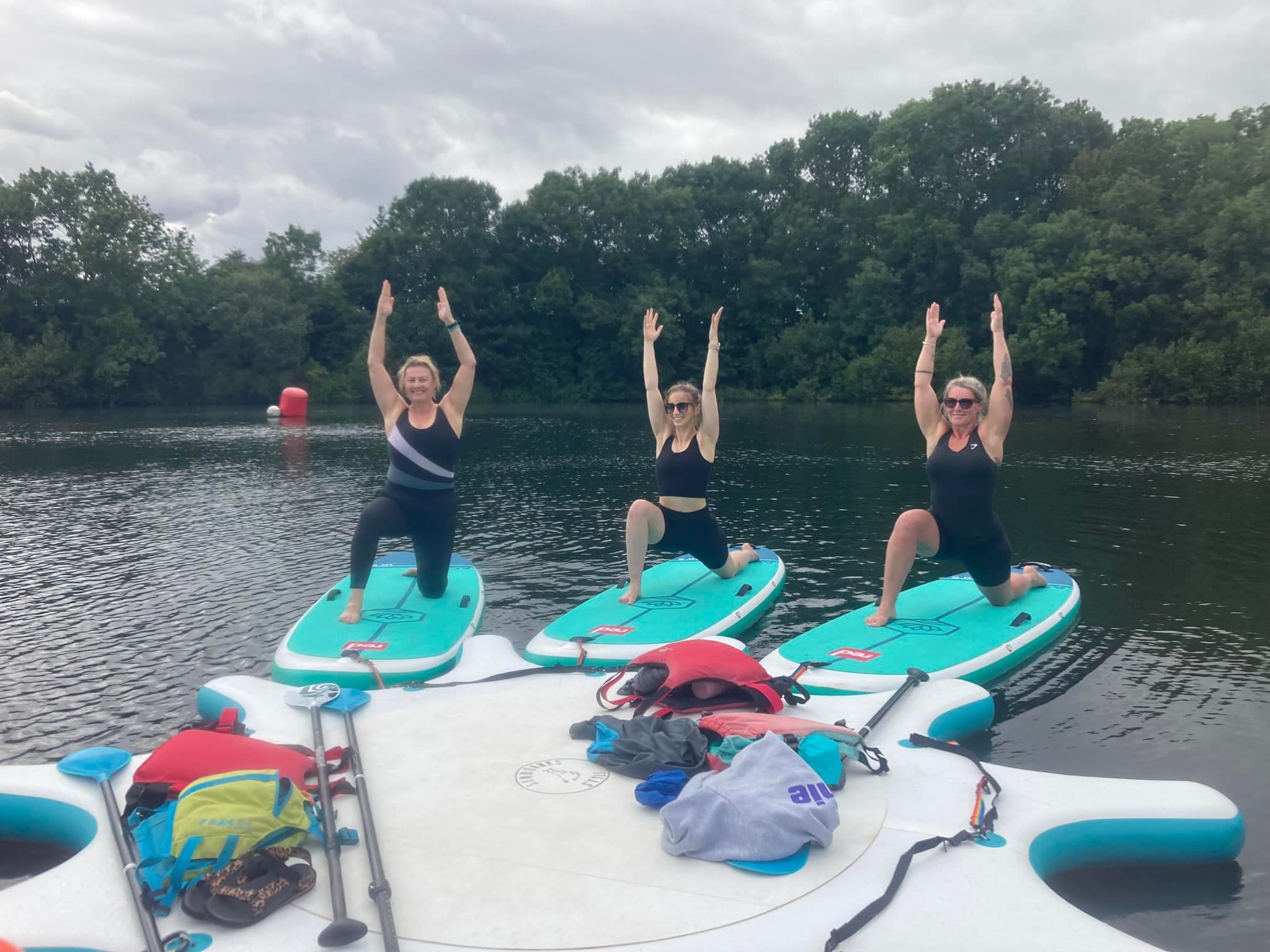 Three women doing paddleboard yoga on inflatable platform on lake