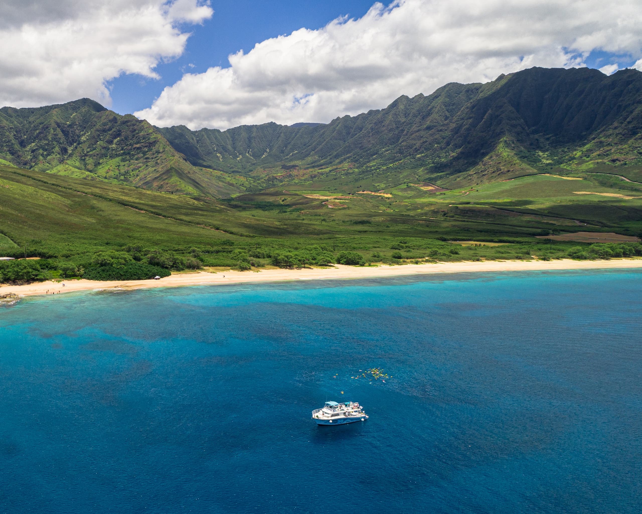 Aerial coastal panorama with boat near lush mountains and reef