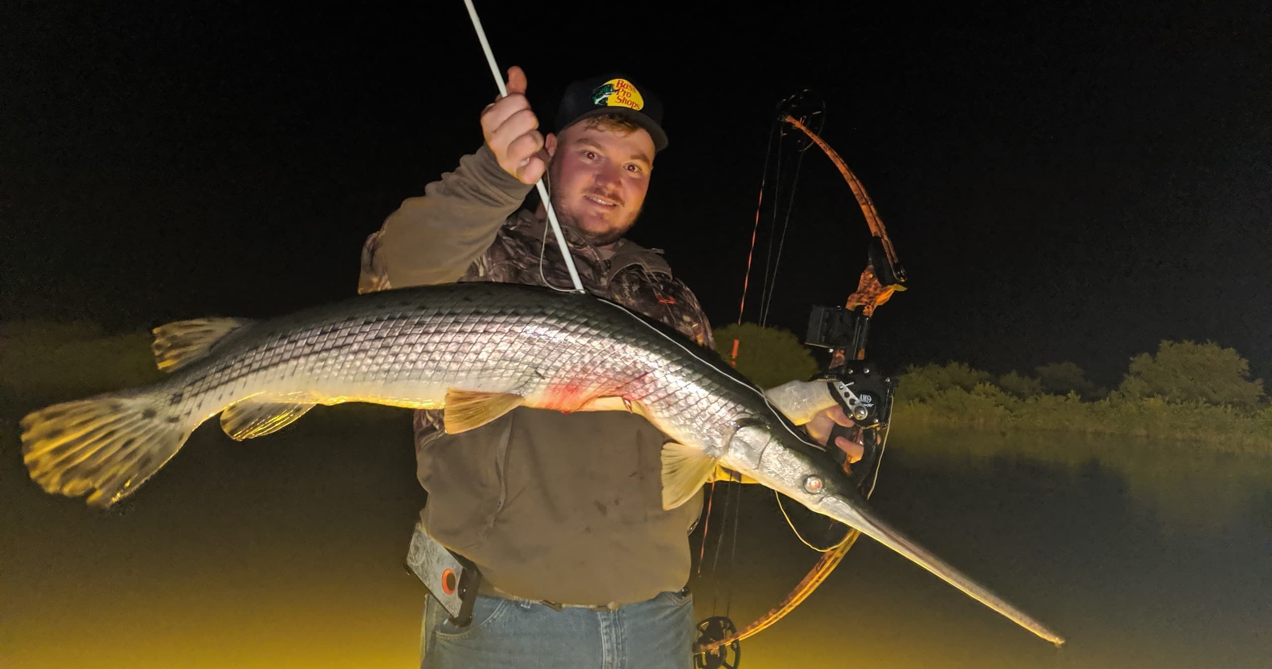 Bowfishing angler holding a long gar at night in Florida