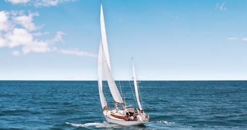 White sailboat cruising open ocean under blue skies