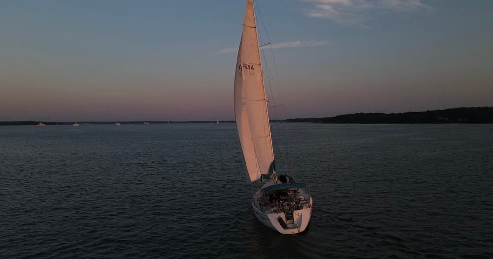 Single sailboat gliding at dusk over open water, aerial view