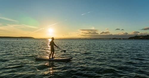 Stand-up paddleboarder silhouetted at sunset on open sea