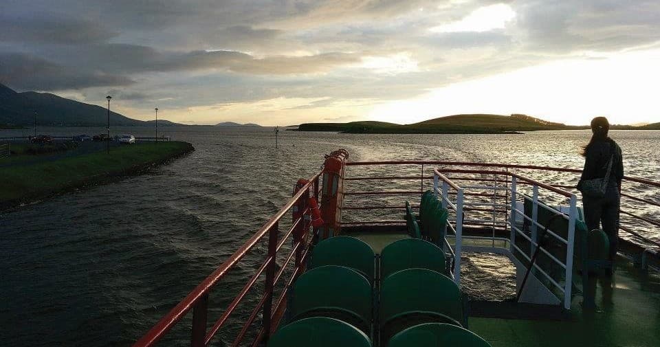 Passengers on ferry deck at sunset crossing coastal channel
