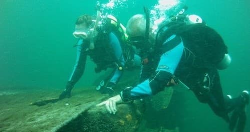 Scuba divers exploring underwater wreck on green temperate seafloor