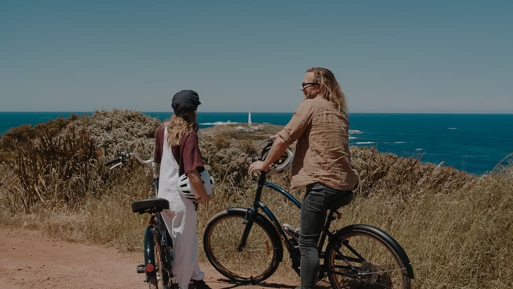 Two cyclists chatting with ocean cliff backdrop on coastal trail