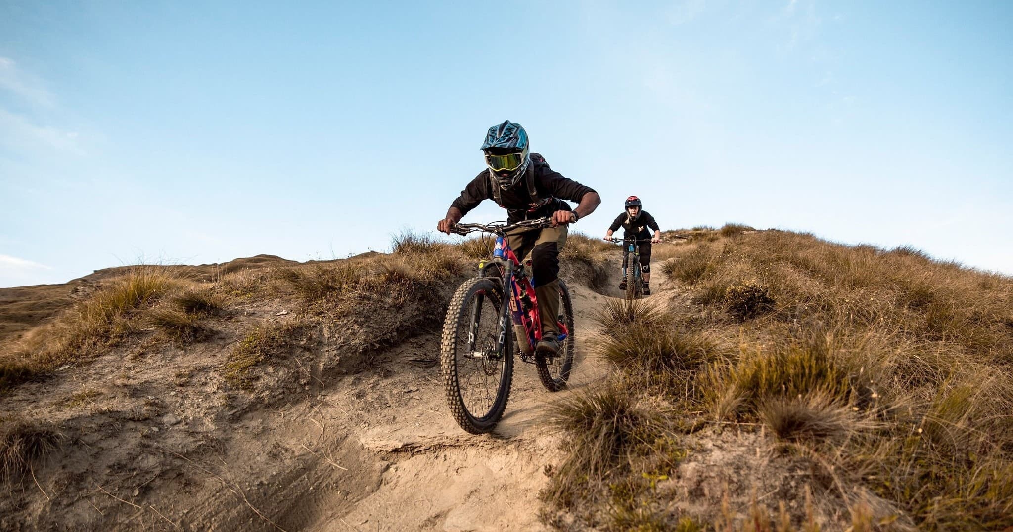 Cyclist charging down singletrack trail toward camera in mountains NZ